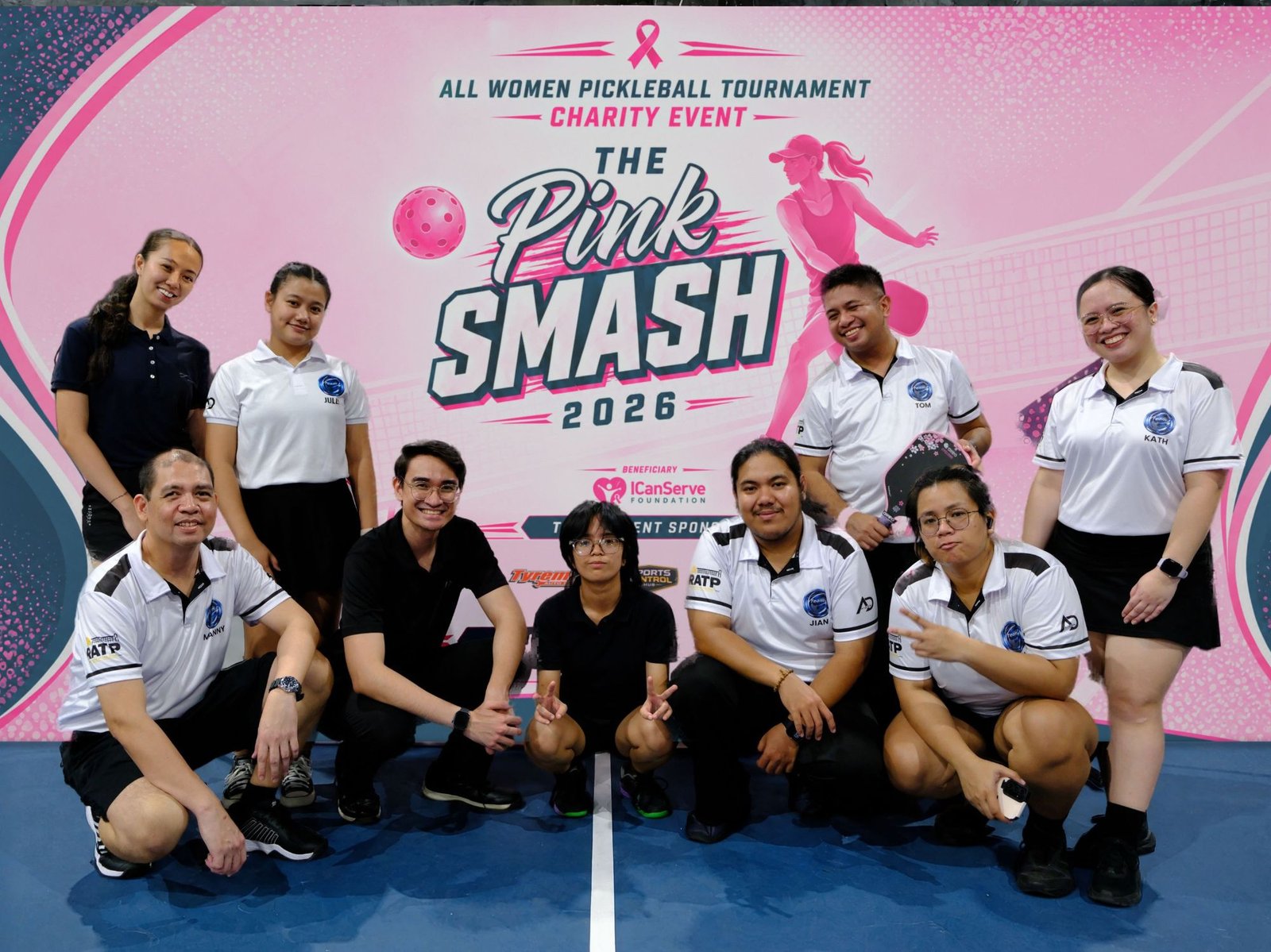The Team J officiating crew posing on court in front of the Pink Smash 2026 backdrop